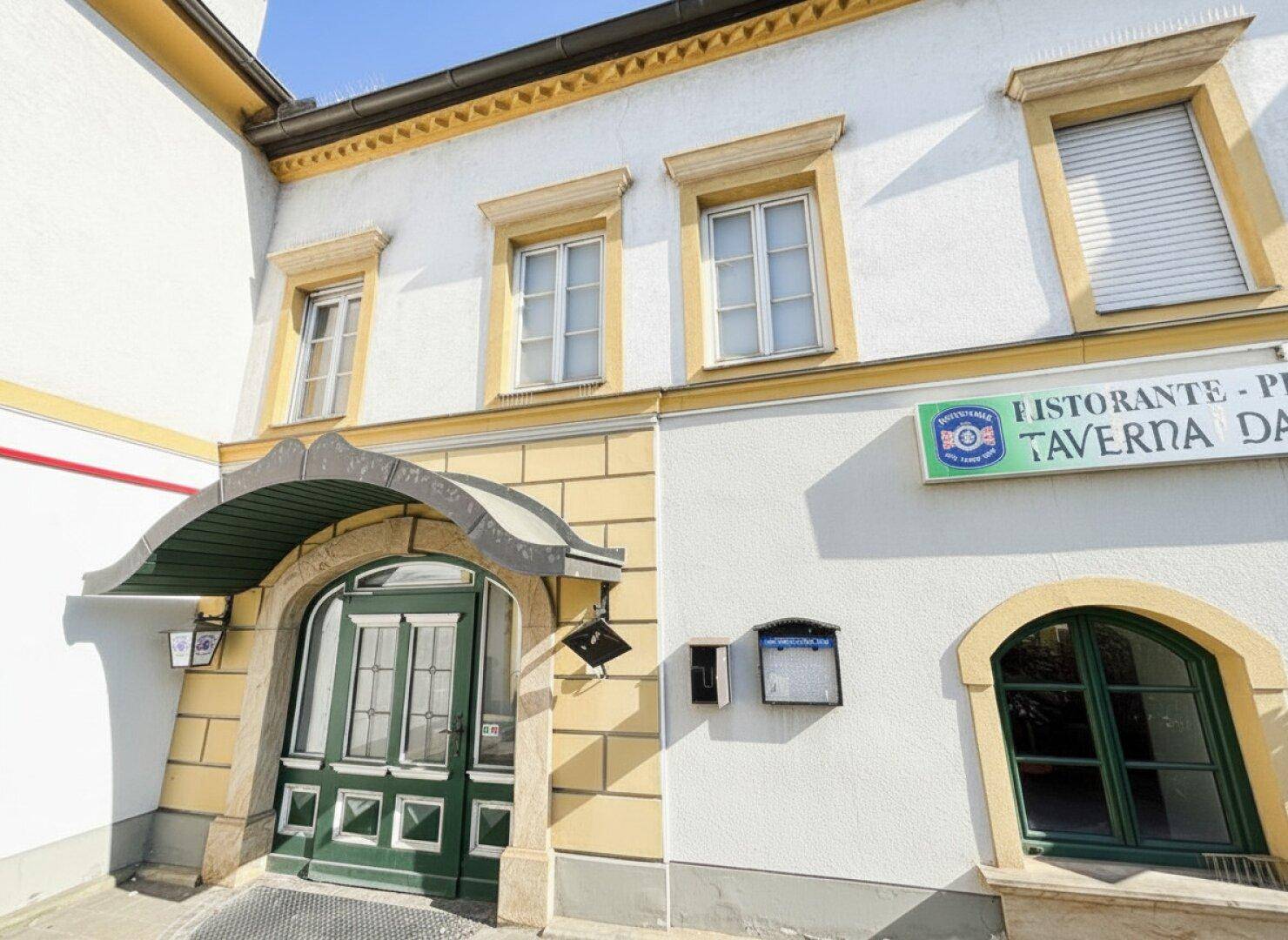 Detaillierte Ansicht des Haupteingangs mit grüner Doppeltür und den Fenstern der oberen Etagen des historischen Gebäudes.