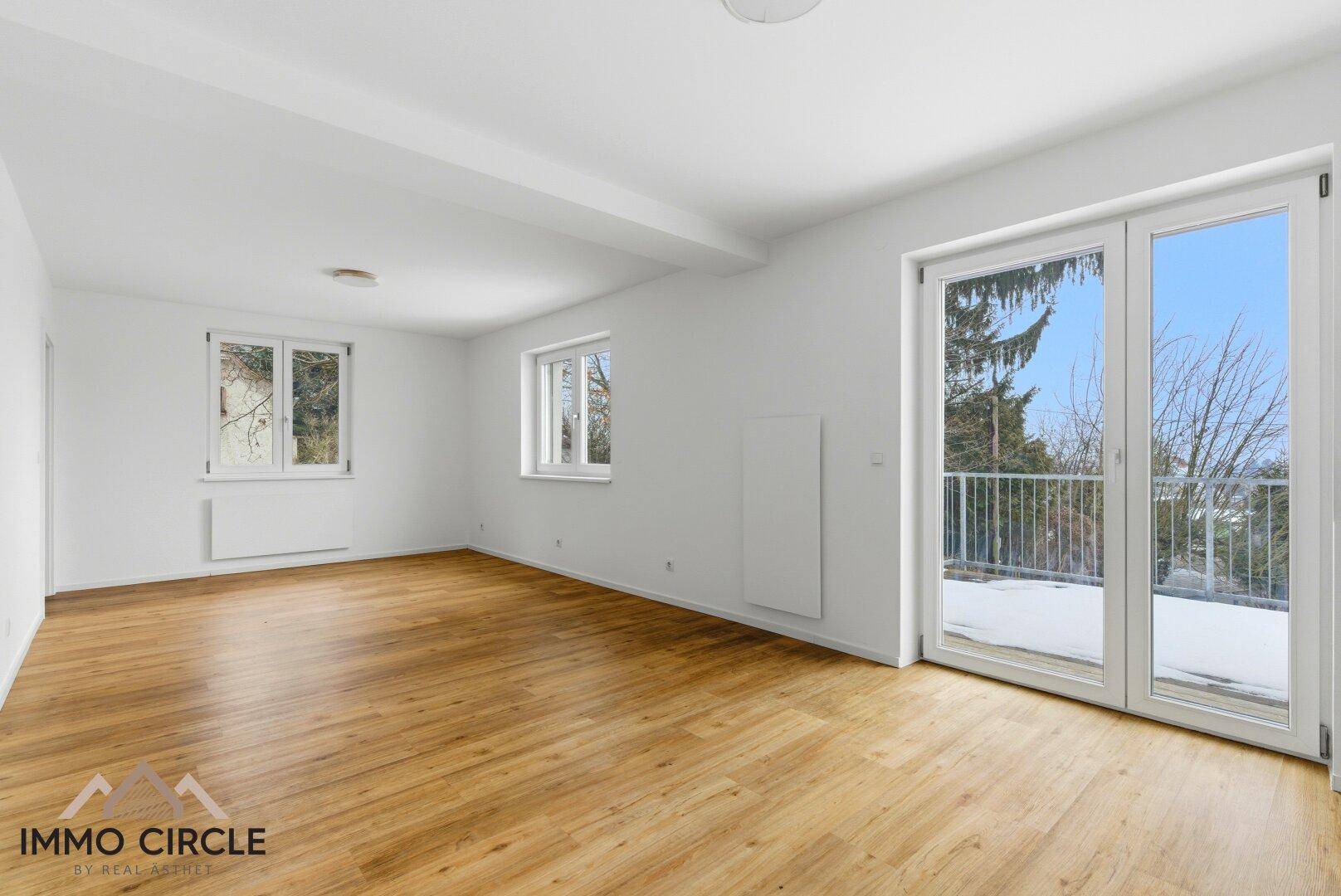 Geräumiges, helles Zimmer mit Holzboden und Zugang zu einem Balkon, ideal als Wohnbereich.