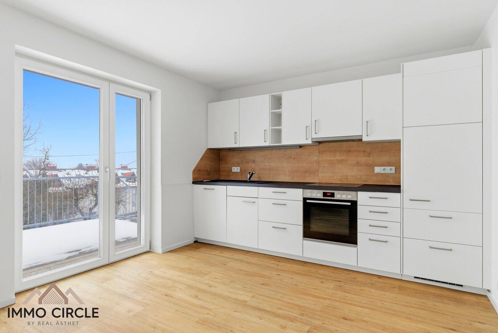 Moderne Einbauküche mit weißen Schränken, Holzarbeitsplatte und Zugang zum Balkon.