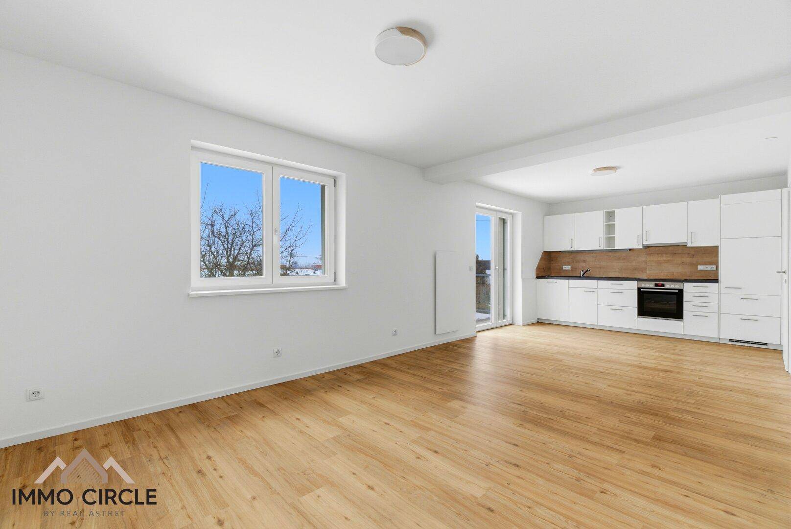 Offener Wohnbereich mit integrierter Küche, Holzboden und viel Tageslicht, ideal für modernes Wohnen.