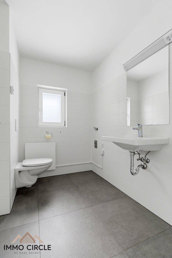 Modernes Badezimmer mit weißen Fliesen, wandhängendem WC und Waschbecken, ausgestattet mit Fenster.