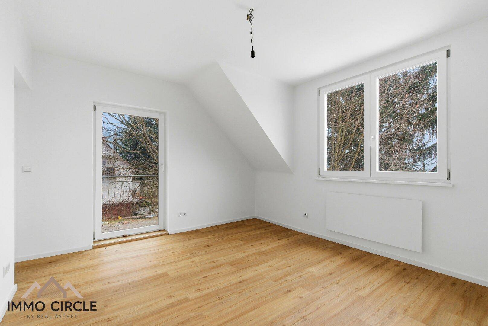 Helles Dachgeschosszimmer mit Holzboden und Zugang zu einem kleinen Balkon, ideal als Schlafzimmer.