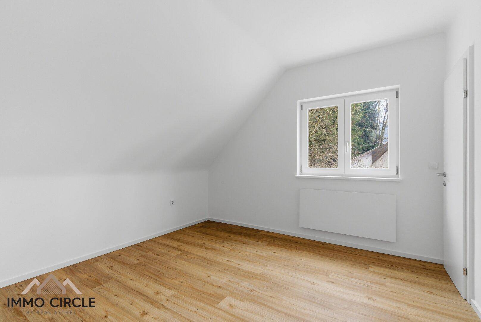 Gemütliches Schlafzimmer im Dachgeschoss mit Holzboden und schrägen Wänden, bietet viel Tageslicht.