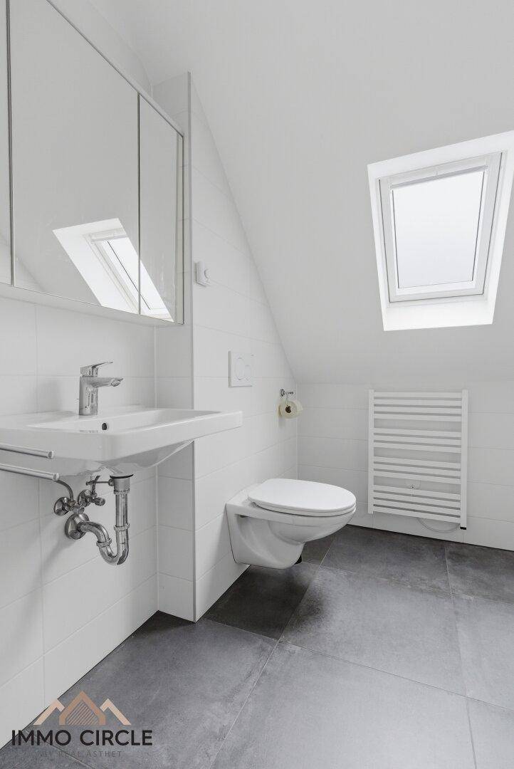 Modernes Badezimmer im Dachgeschoss mit Dachfenster, wandhängendem WC und Waschbecken.