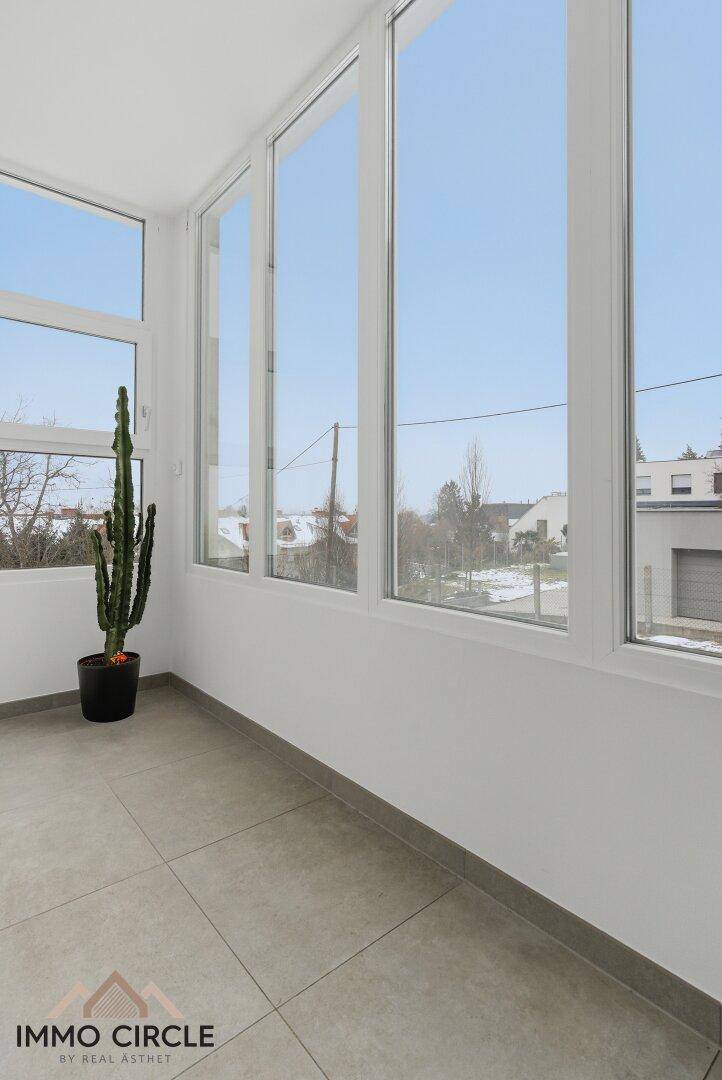 Heller Wintergarten mit großen Fenstern und Fliesenboden, bietet einen weiten Blick nach draußen.
