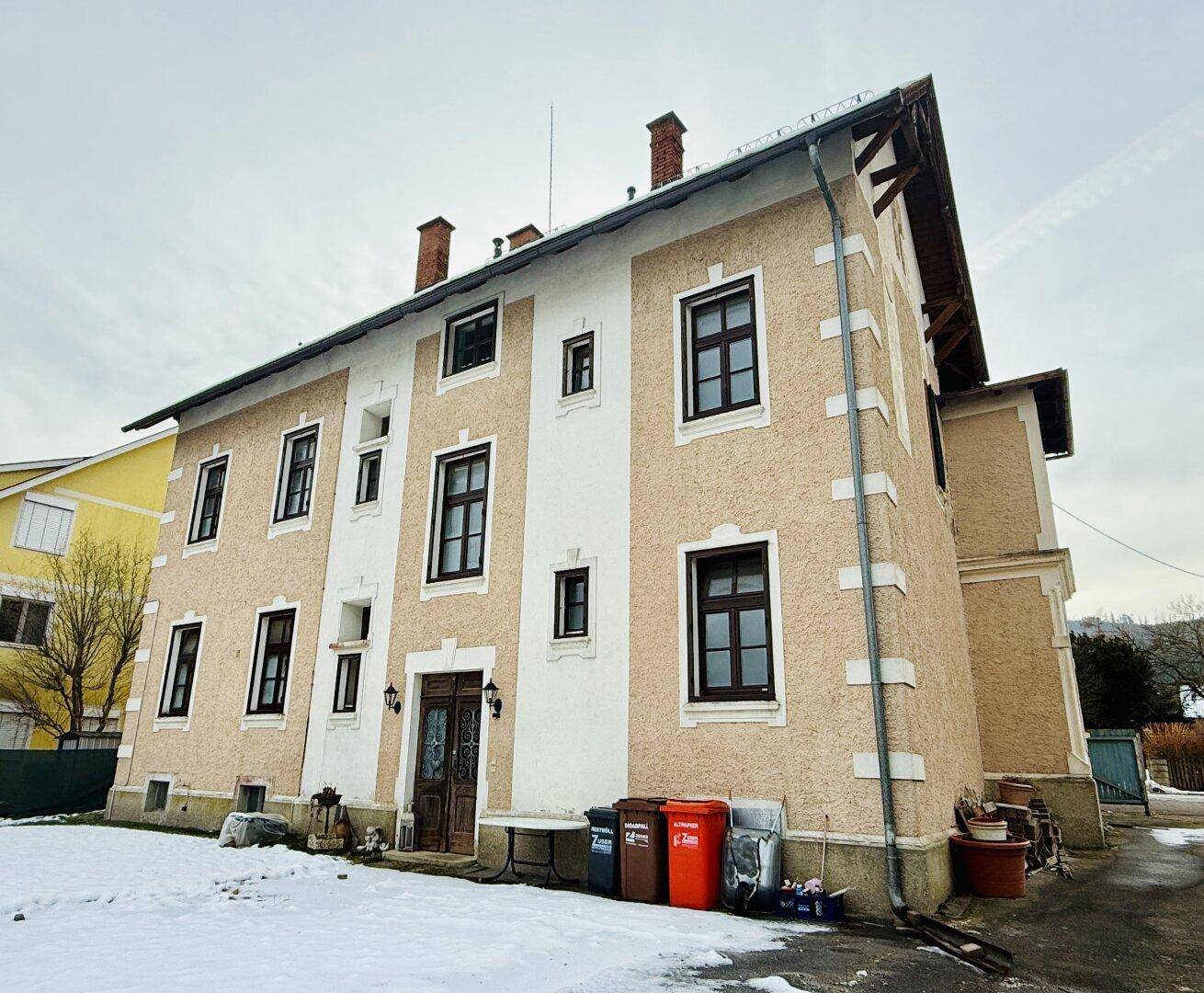 Seitenansicht des Gebäudes mit mehreren Fenstern, traditioneller Fassade und Schnee im Vorgarten.