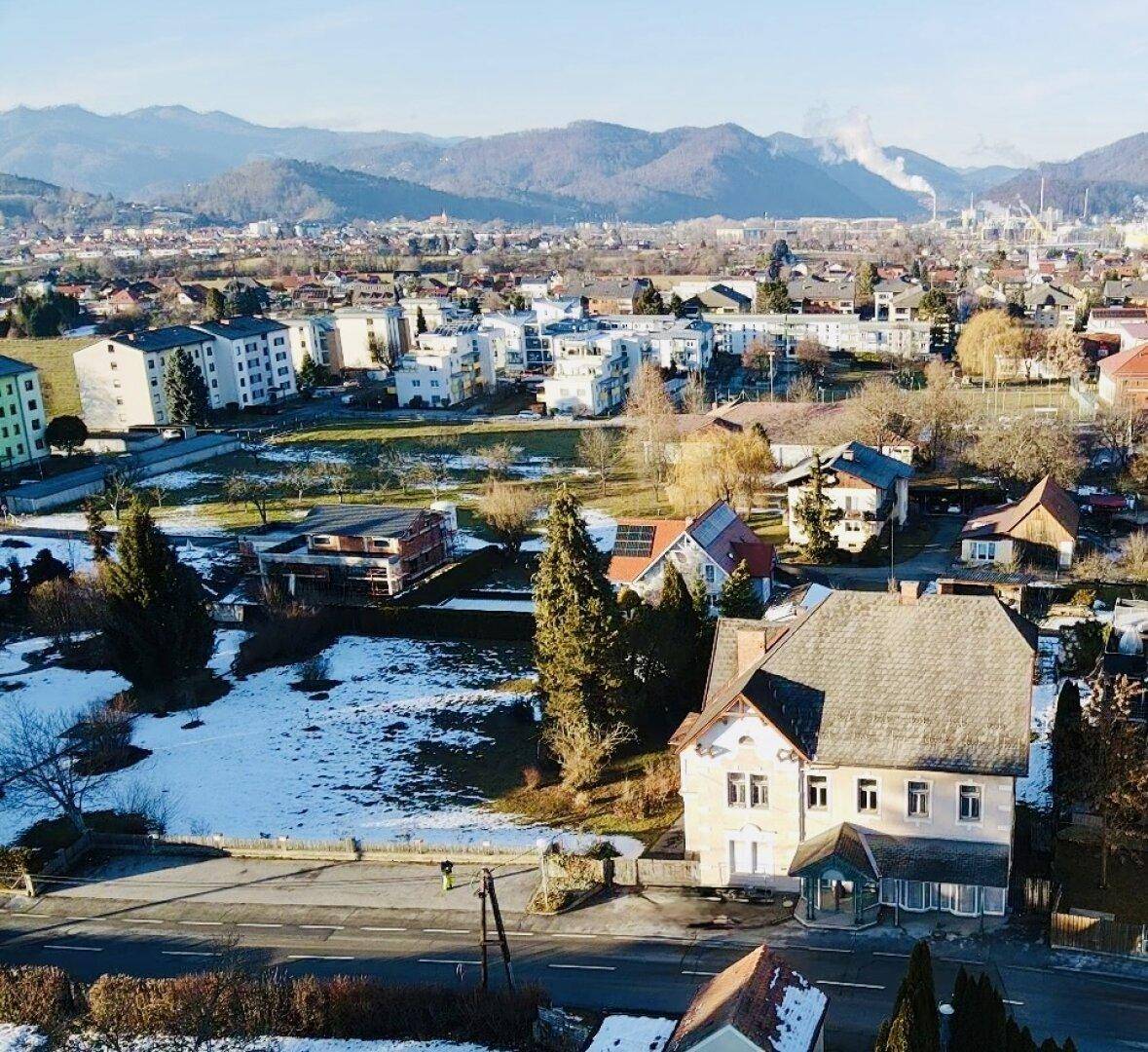 Weitläufiger Blick über die Stadt und die umliegende Berglandschaft mit dem Gebäude im Vordergrund.