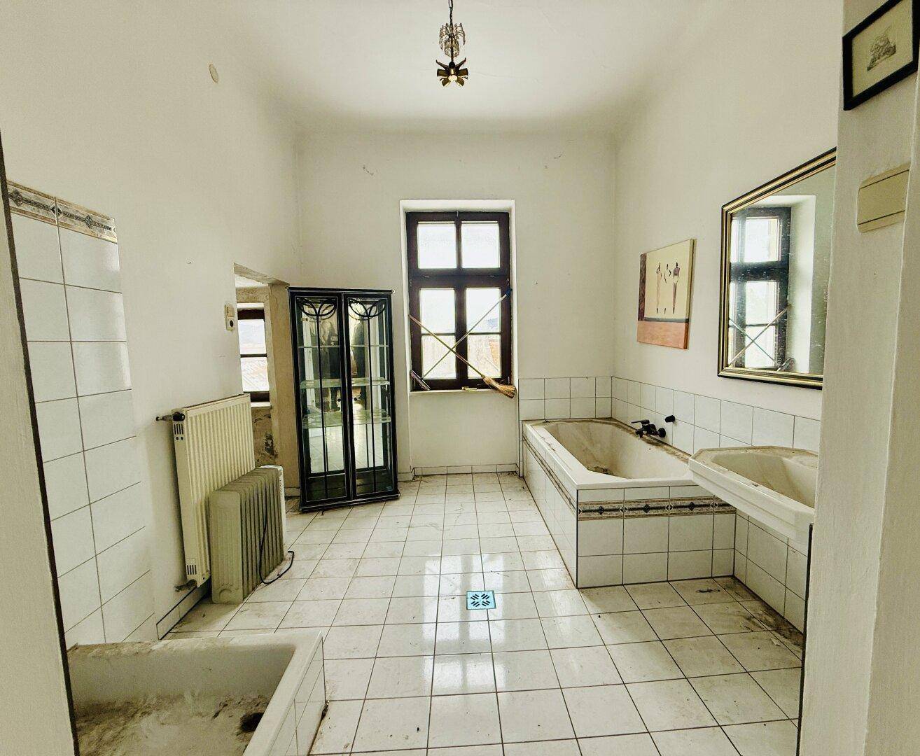 Geräumiges Badezimmer mit Badewanne, Waschbecken und Fliesenboden, das eine Renovierung benötigt.