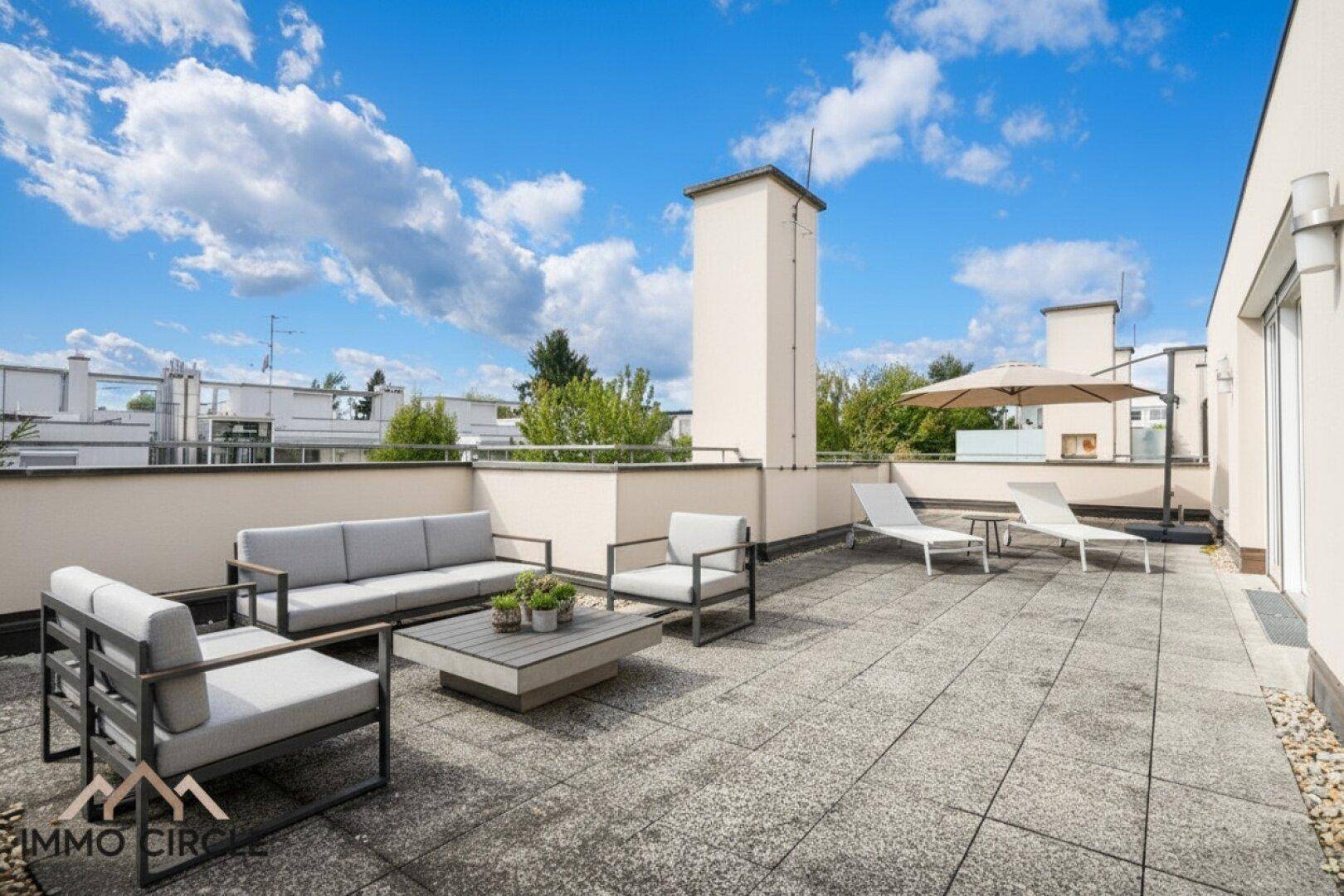 Geräumige Dachterrasse mit moderner Lounge-Möblierung, Sonnenliegen und Sonnenschirm unter blauem Himmel.