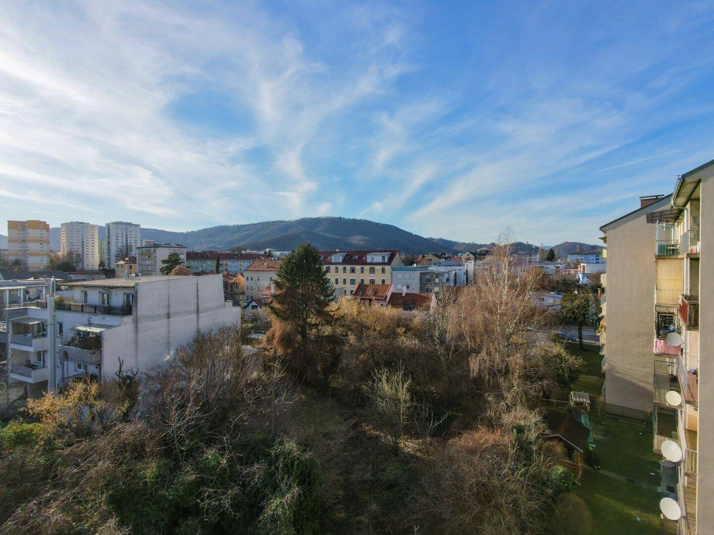 Panoramablick über die Stadt mit Bergen im Hintergrund unter blauem Himmel.