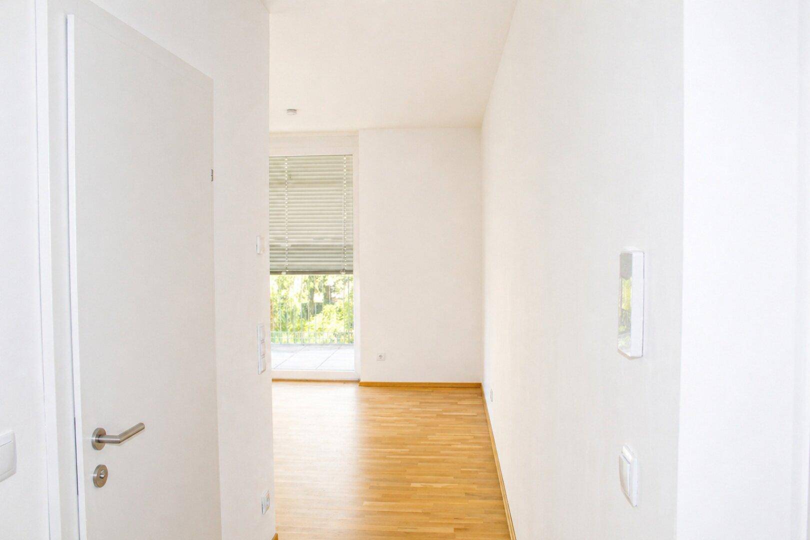 Heller Flur mit Holzboden und weiß gestrichenen Wänden, führt zu einem weiteren Raum.
