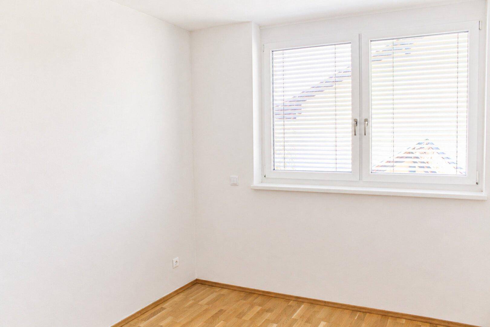 Leerer Raum mit Holzboden und einem Fenster mit Jalousien, ideal als Schlaf- oder Arbeitszimmer.