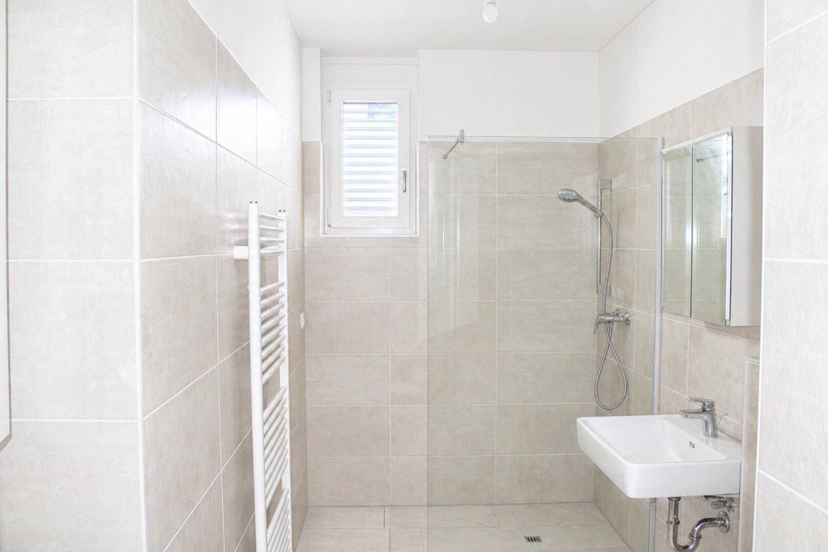Modernes Badezimmer mit beigefarbenen Fliesen, ebenerdiger Dusche und beheiztem Handtuchhalter.