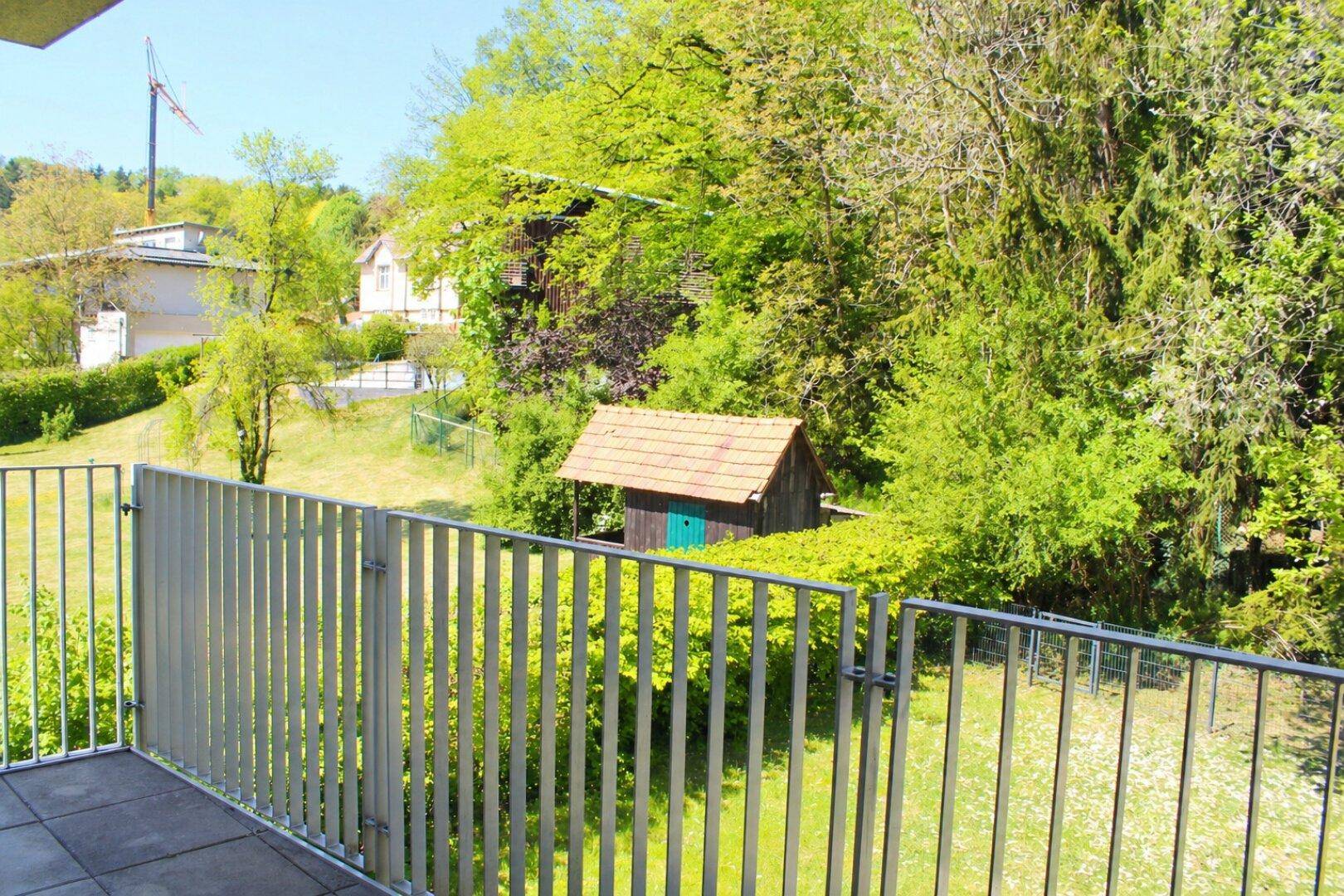 Balkon mit Blick auf einen kleinen Gartenschuppen und üppiges Grün in der Umgebung.