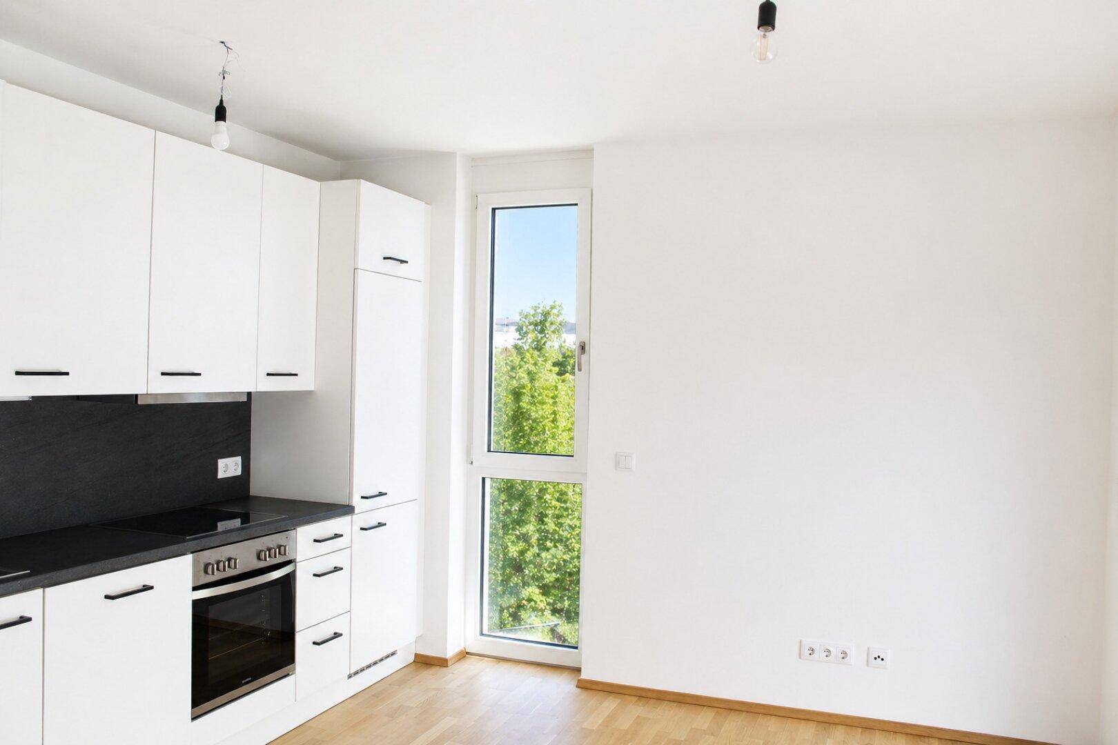 Funktionale Küche mit weißen Schränken und Holzboden, bietet viel Stauraum und Tageslicht.