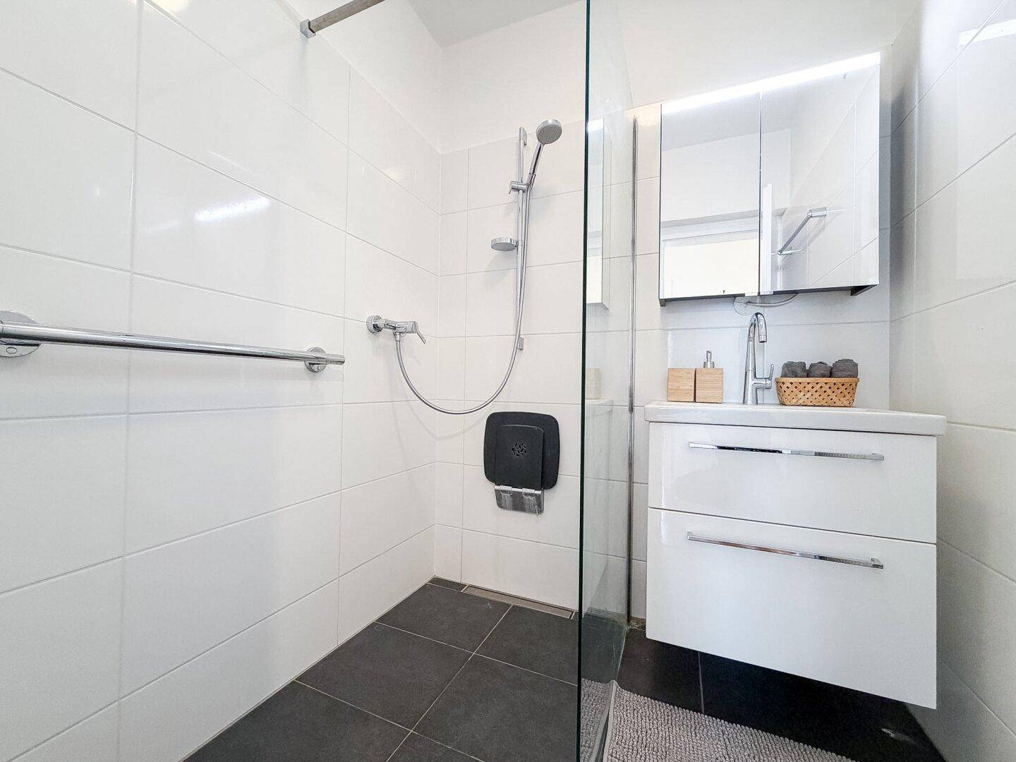 Modernes Badezimmer mit ebenerdiger Dusche, weißen Fliesen und Waschtisch.