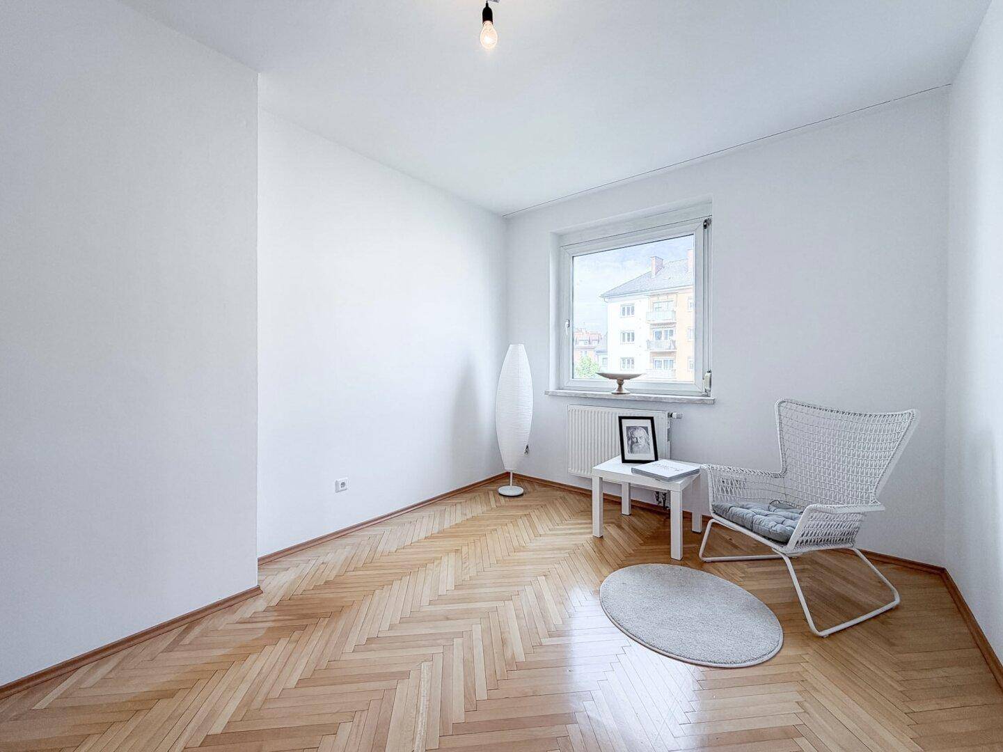Geräumiges Zimmer mit Fischgrätparkett und viel Tageslicht durch das Fenster.