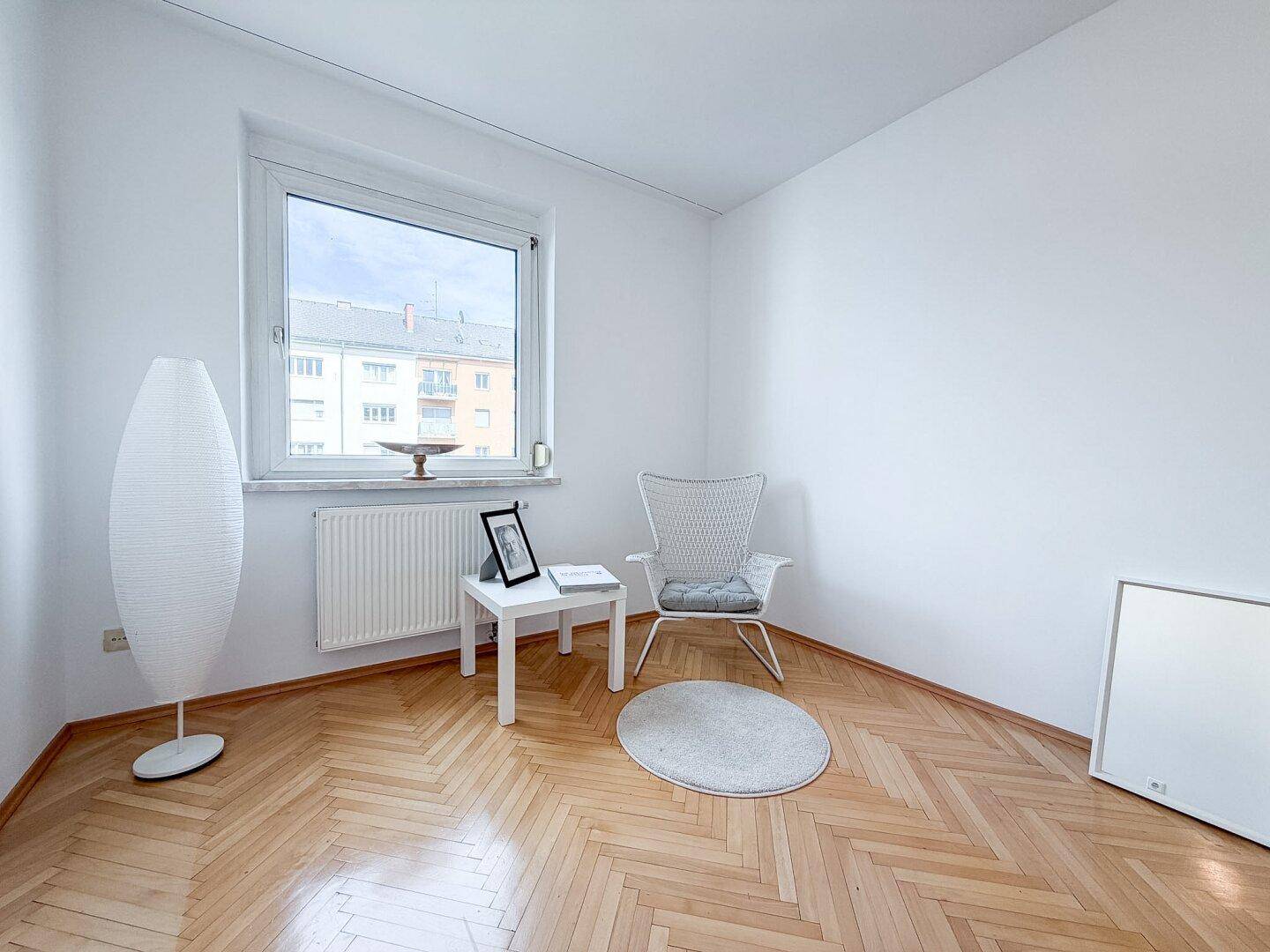 Helles Zimmer mit Fischgrätparkett, großem Fenster und gemütlicher Sitzecke.