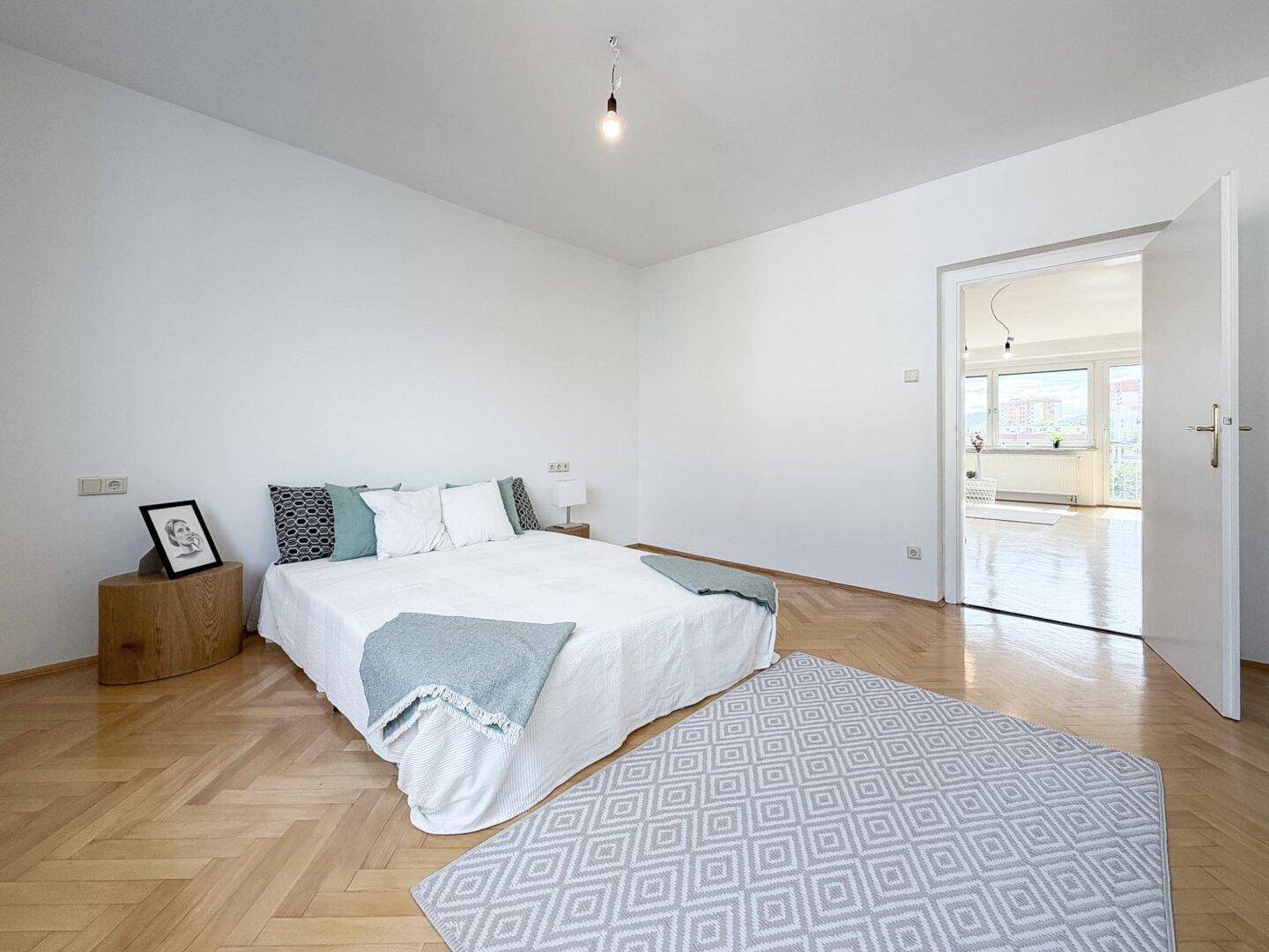 Geräumiges Schlafzimmer mit Fischgrätparkett und offenem Zugang zum Wohnbereich.