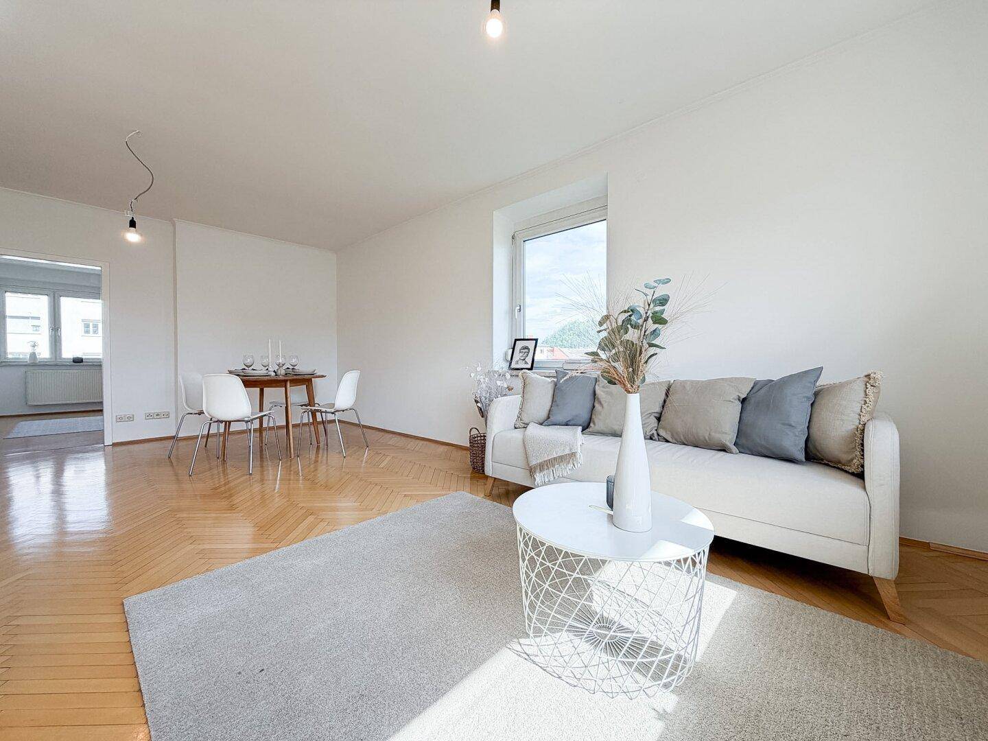 Gemütlicher Wohnbereich mit Sofa, Couchtisch und Essbereich im Hintergrund.