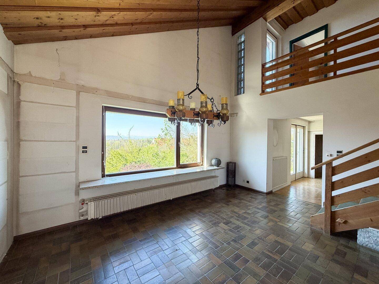 Helles Wohnzimmer mit großem Fenster, Holzbalkendecke und Blick ins Grüne.
