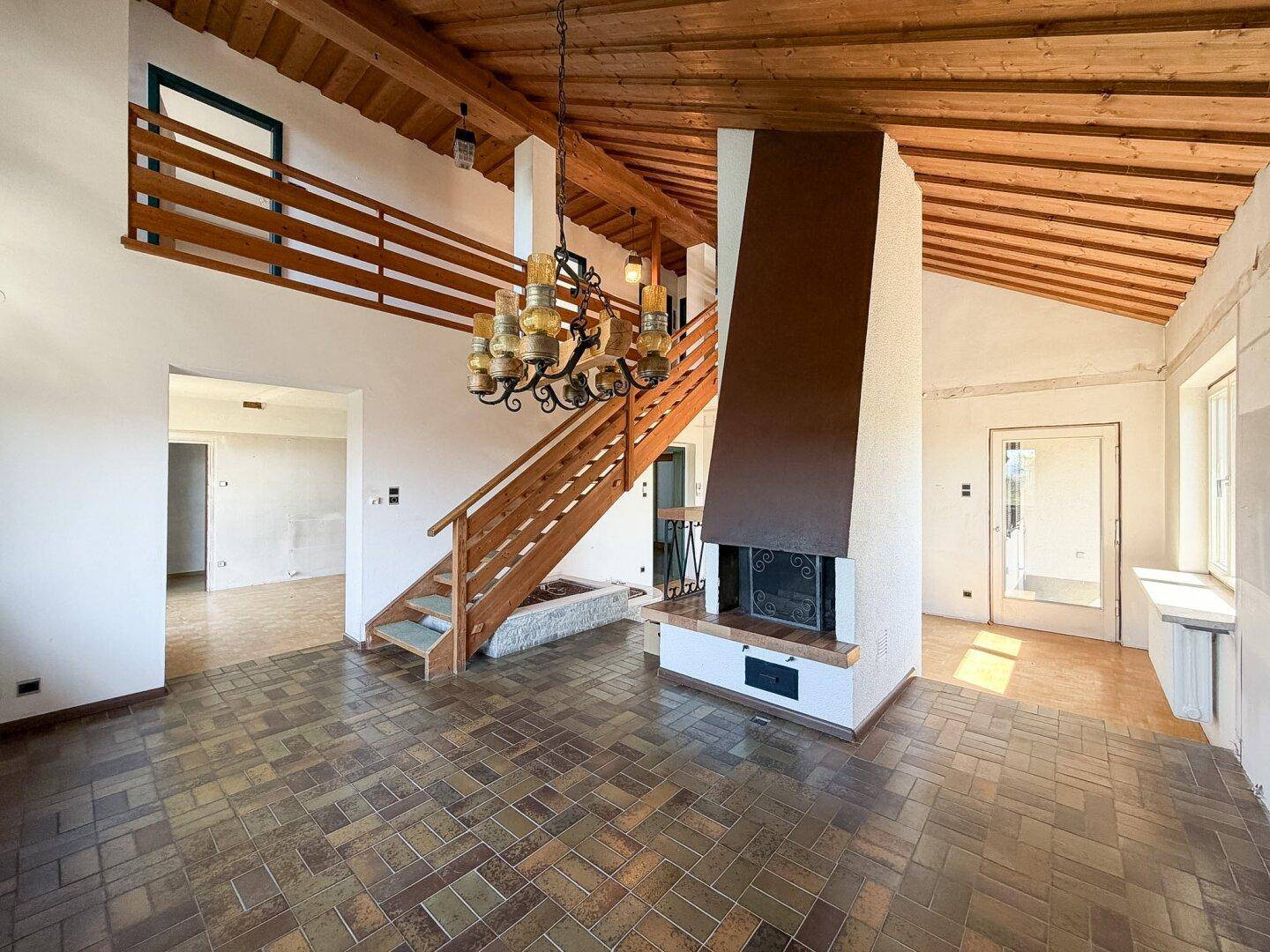 Geräumiges Wohnzimmer mit Holzbalkendecke, Kamin und gefliestem Boden.