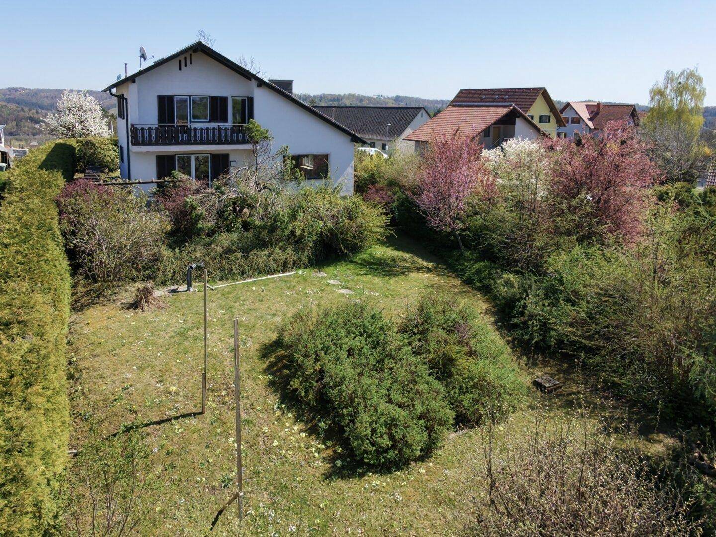 Gartenbereich mit Sträuchern und Rasenfläche, im Hintergrund das Haus mit Balkon.