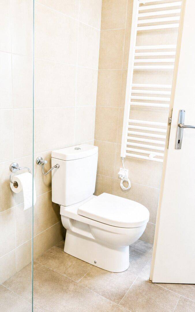 Modernes Badezimmer mit Toilette, beheiztem Handtuchhalter und hellen Fliesen.