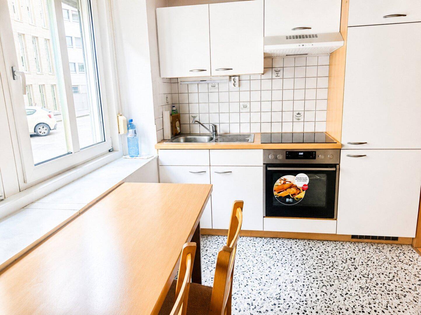 Helle Küche mit weißen Schränken, integrierten Geräten und einem Esstisch am Fenster.