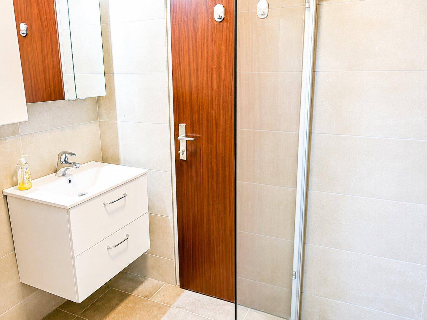 Badezimmer mit modernem Waschtisch, Spiegelschrank und Duschbereich mit Glaswand.