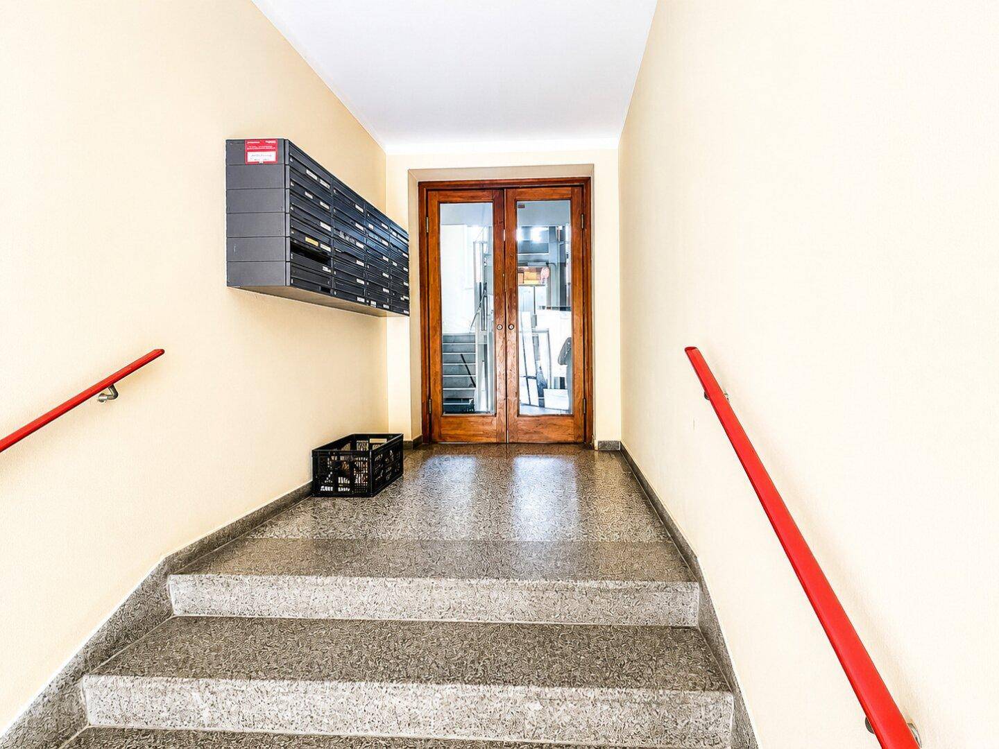 Eingangsbereich mit Treppe, Briefkästen und einer Holztür, die zum Treppenhaus führt.