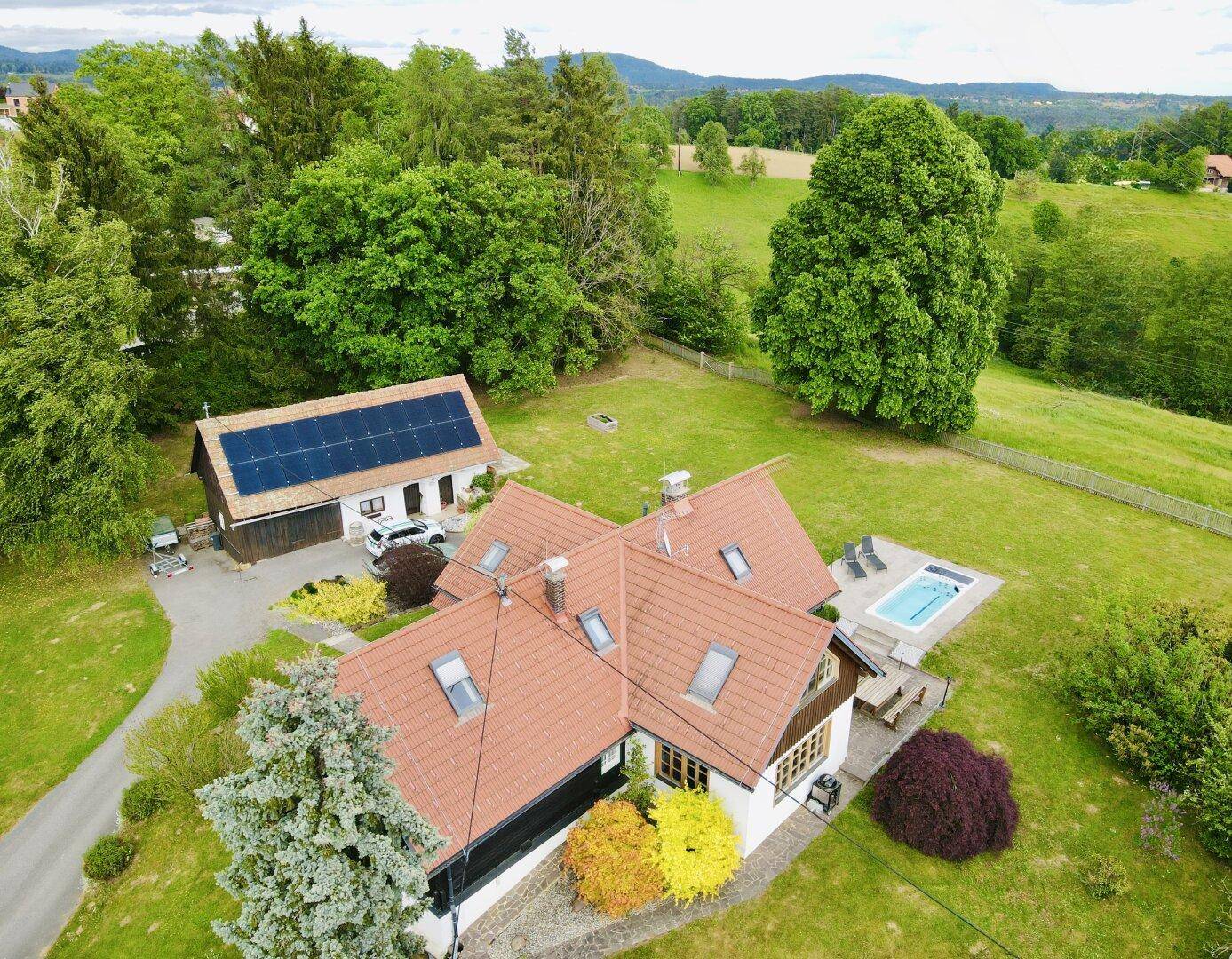 Vogelperspektive eines Anwesens mit Haupthaus, Poolbereich und Nebengebäude mit Photovoltaikmodulen.