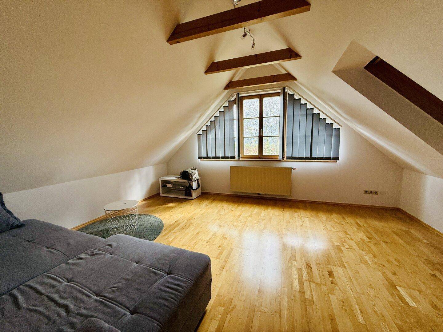 Helles Dachzimmer mit schrägen Wänden, Holzboden und einem bequemen Sofa.