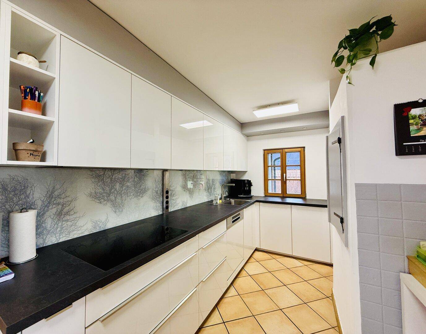 Moderne Küche mit weißen Hochglanzschränken, dunkler Arbeitsplatte und gefliestem Boden.