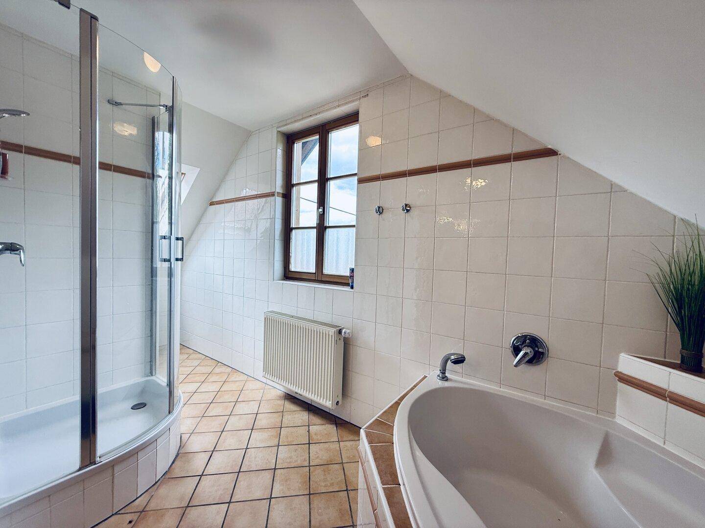 Badezimmer im Dachgeschoss mit Duschkabine, Badewanne, Fenster und gefliesten Wänden.