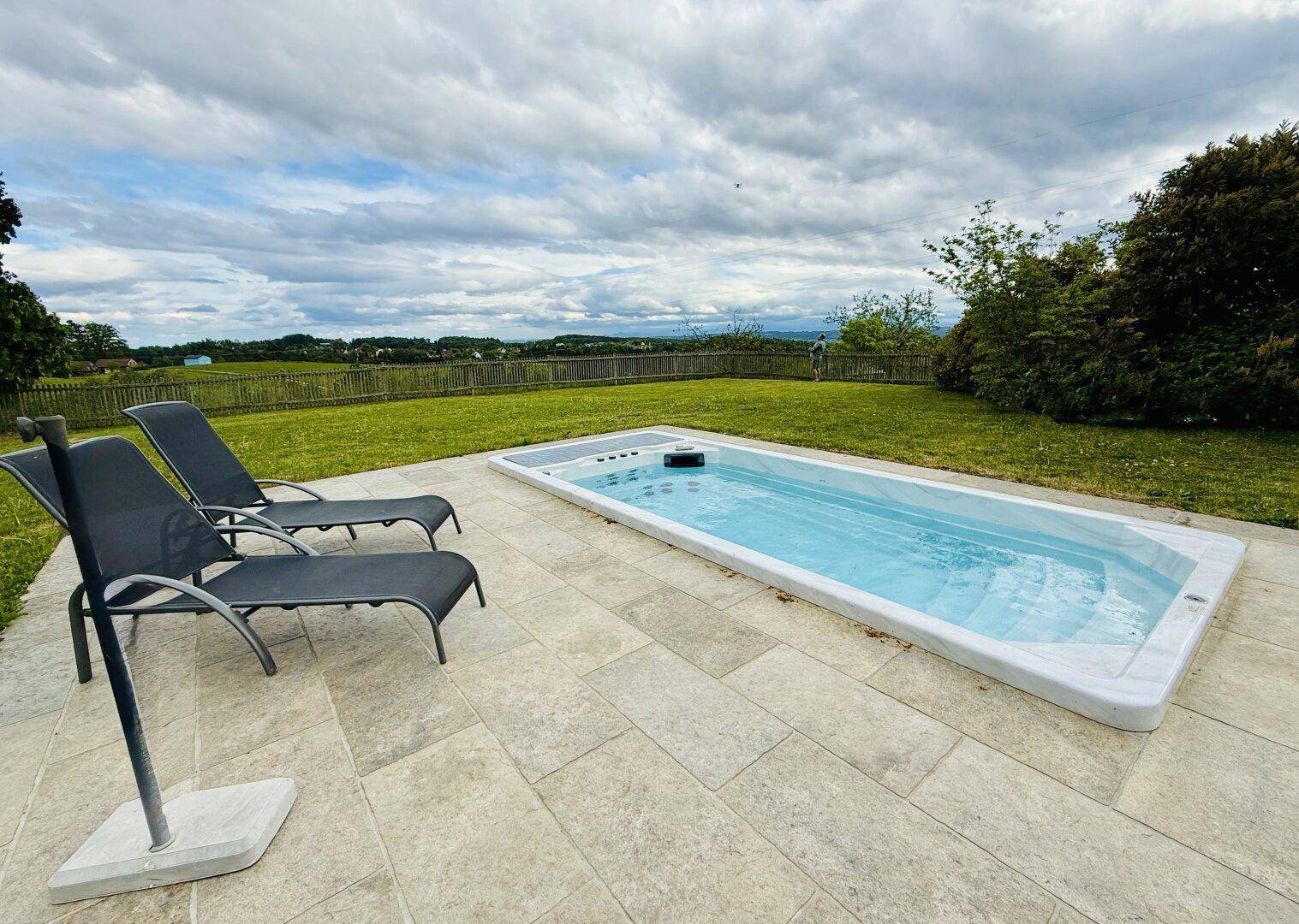 Langer, schmaler Pool mit Liegestühlen auf einer gefliesten Terrasse und weitem Blick in die Landschaft.