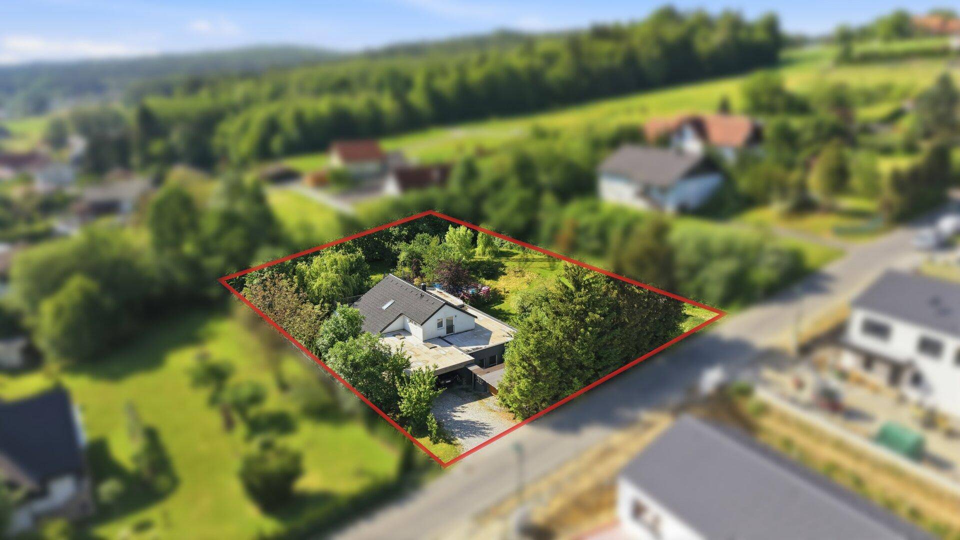 Luftaufnahme des Grundstücks mit markierter Grenze, umgeben von viel Grün und weiteren Häusern.