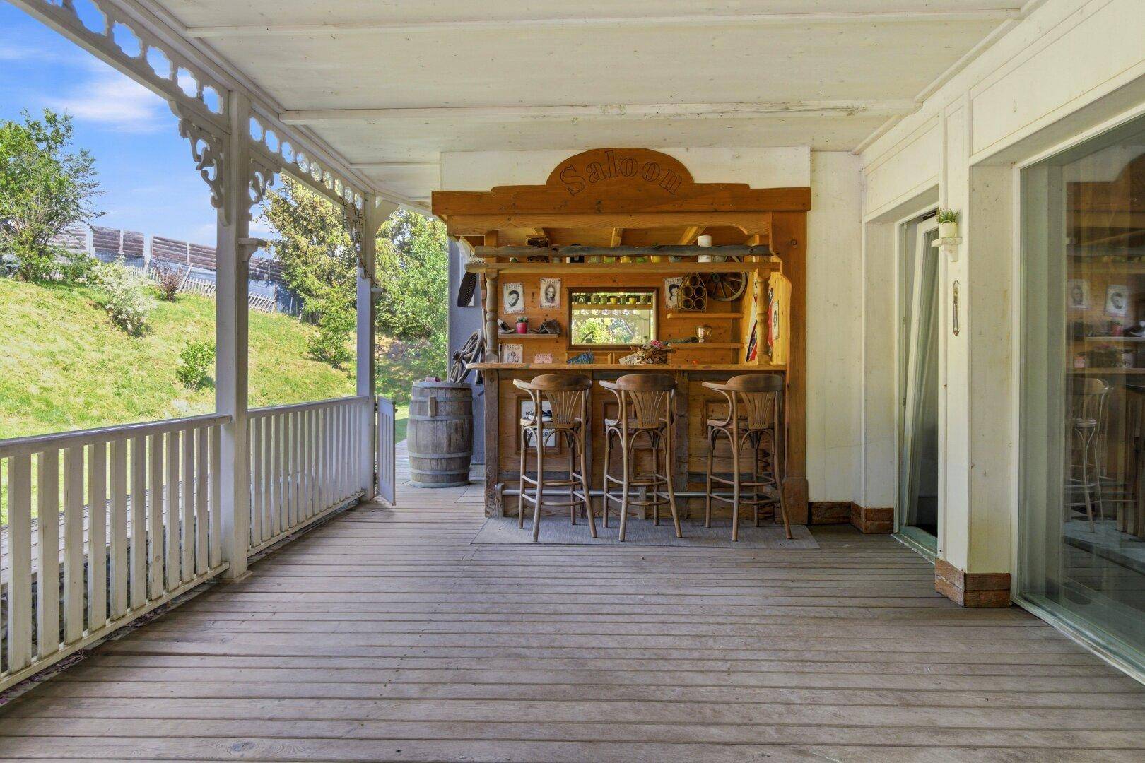Überdachte Holzterrasse mit rustikaler Bar und Hockern, ideal für gesellige Abende.