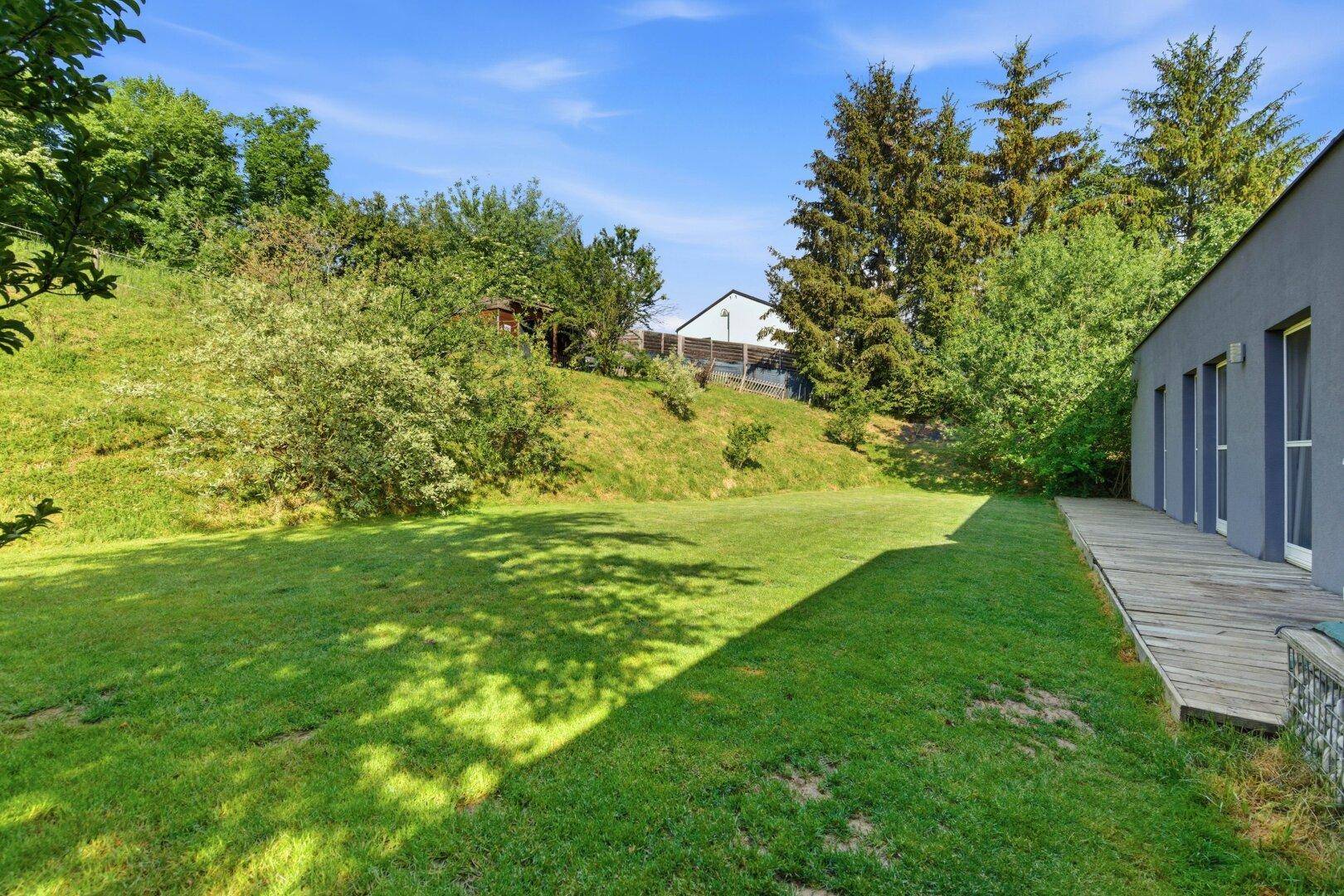 Weitläufiger, leicht abfallender Gartenbereich mit Rasen und Bäumen, ideal zum Entspannen.