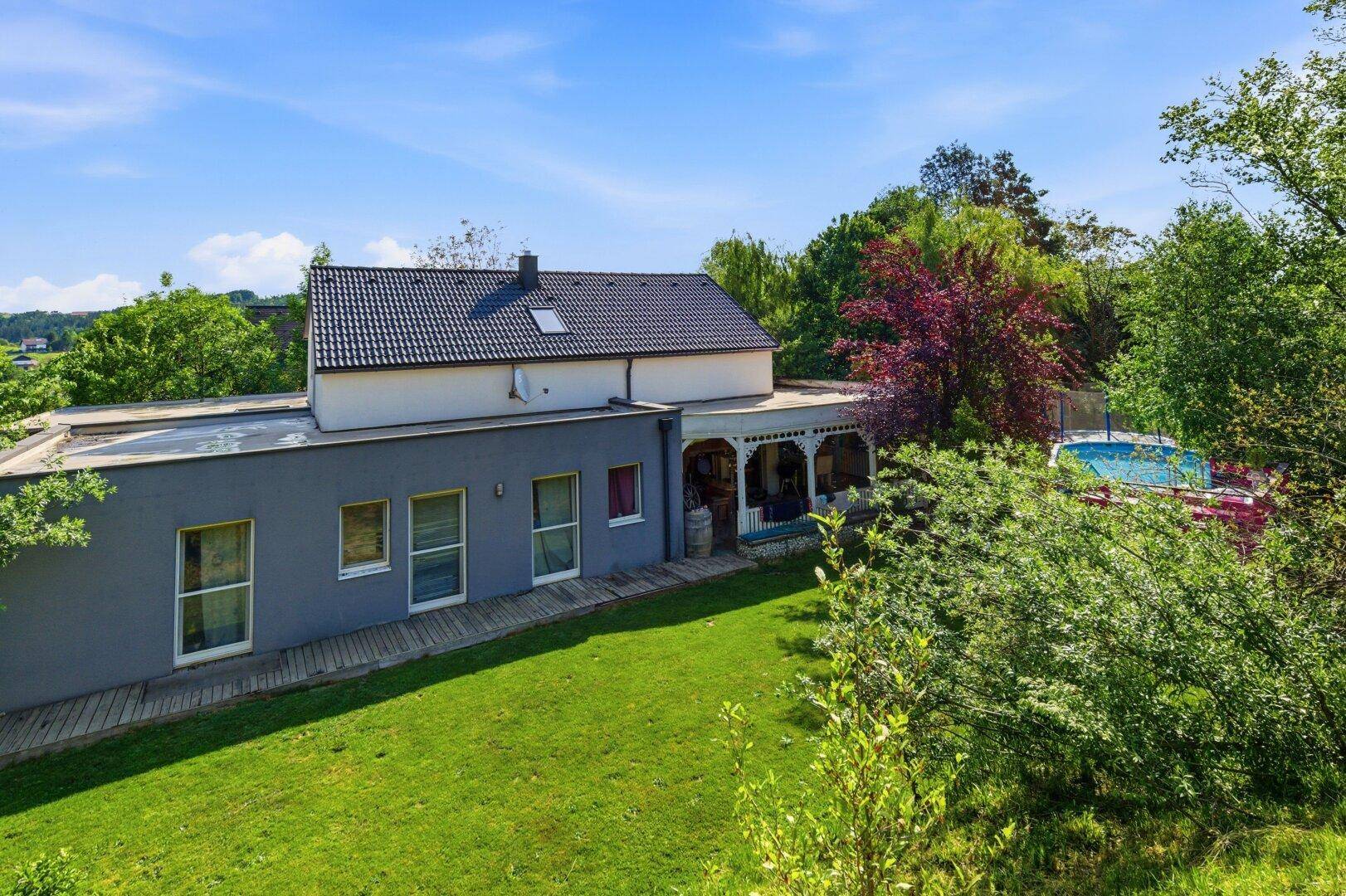 Rückansicht des Hauses mit großem Garten, Pool und überdachter Terrasse im Grünen.