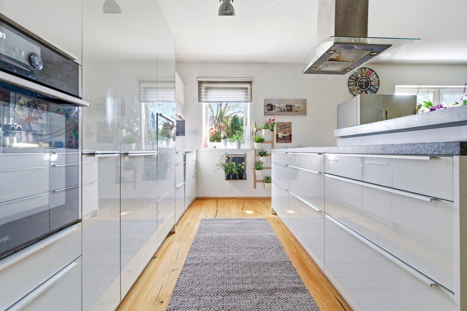 Moderne Küche mit weißen Hochglanzfronten, Holzboden und integrierten Geräten.