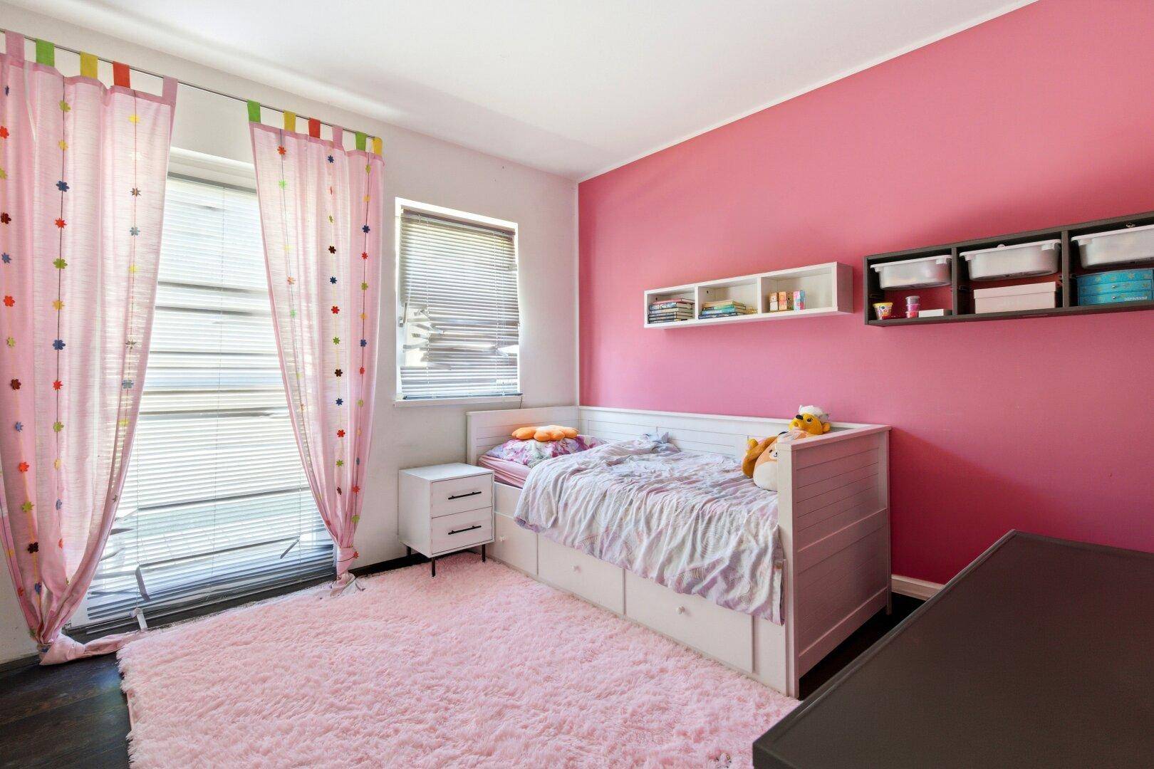 Kinderzimmer mit rosa Wänden, Einzelbett und farbenfrohen Vorhängen.