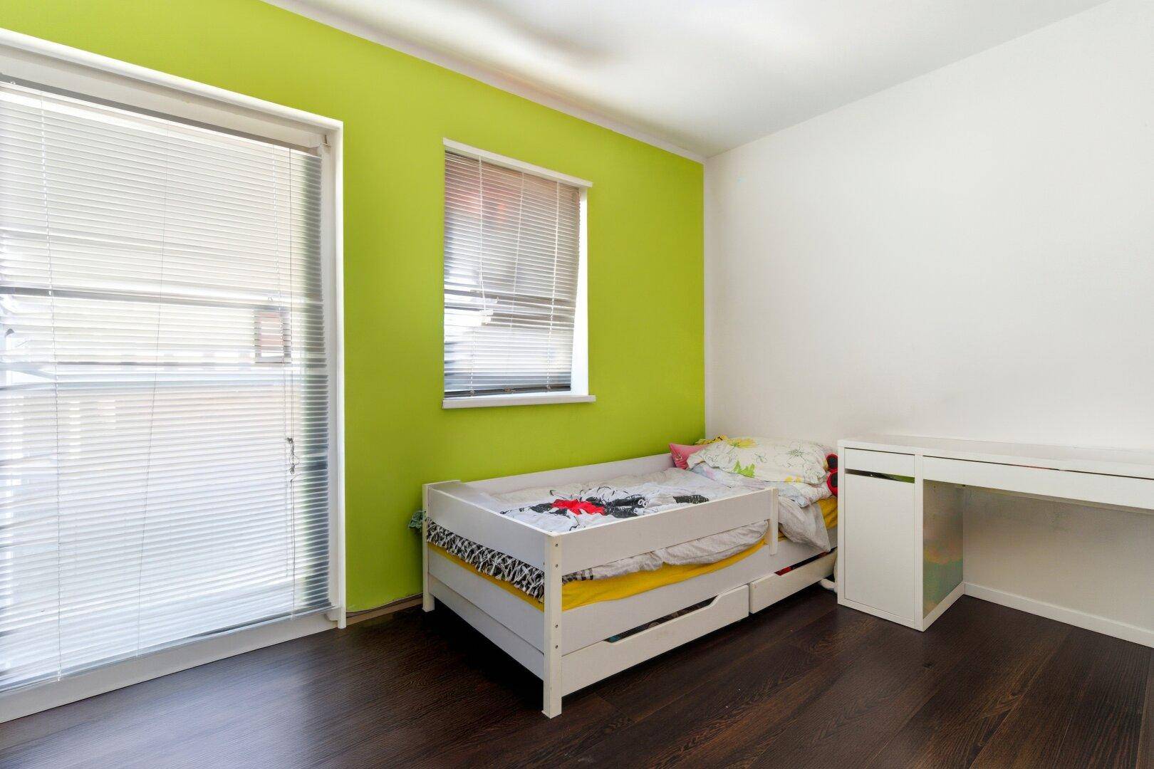 Helles Kinderzimmer mit grüner Akzentwand, Einzelbett und Schreibtisch.