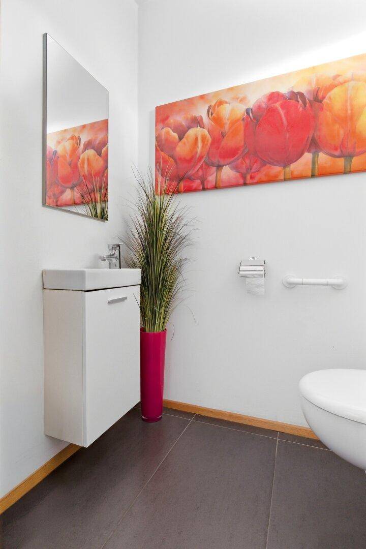 Kleines Gäste-WC mit modernem Waschbecken, Toilette und farbenfrohem Wandbild.