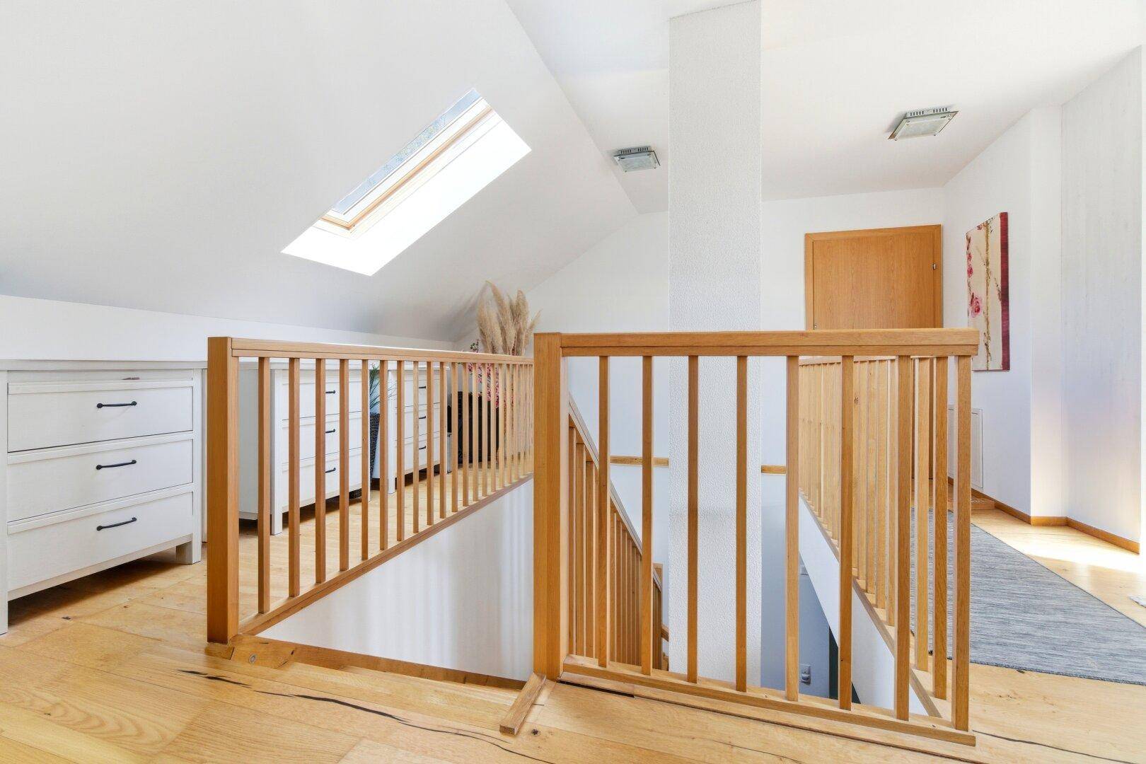 Heller Flur im Obergeschoss mit Holzgeländer, Holzboden und Dachfenster.