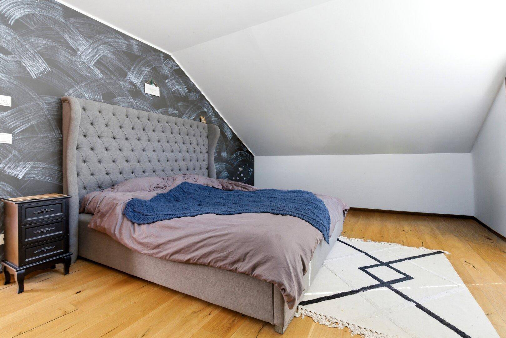 Schlafzimmer im Dachgeschoss mit großem Bett, Holzboden und schräger Decke.