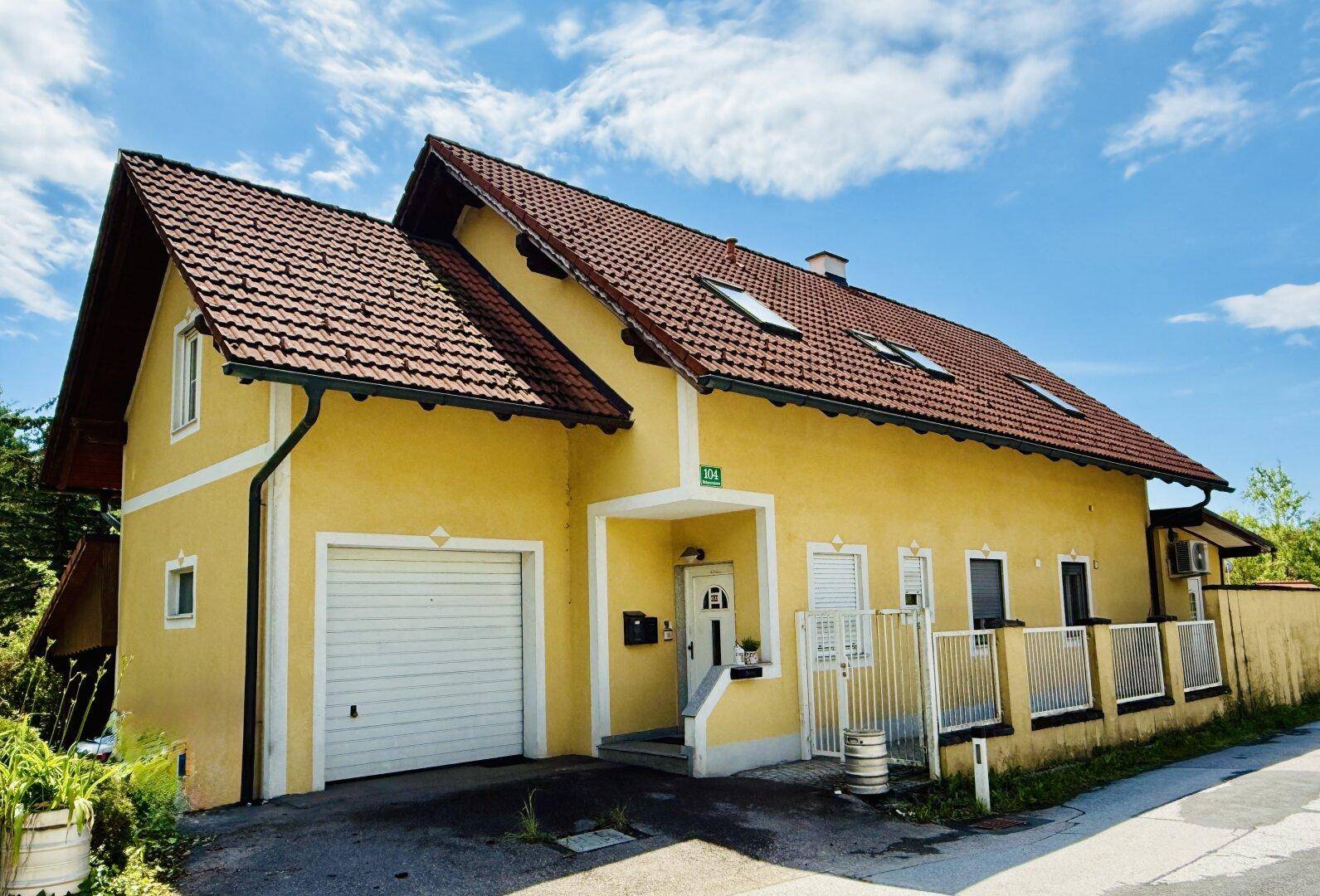 Gelbes Einfamilienhaus mit rotem Ziegeldach, Garage und Vorgarten an einer ruhigen Straße.