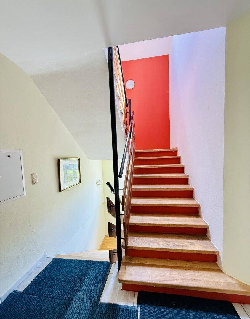 Treppenhaus mit Holzstufen, schwarzem Geländer und einer auffälligen roten Wand.