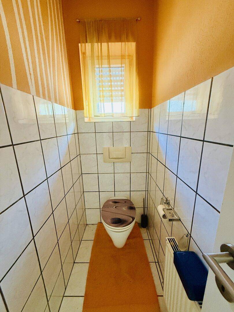 Kleines Gäste-WC mit weißen Fliesen, Fenster und einer orangefarbenen Akzentwand.