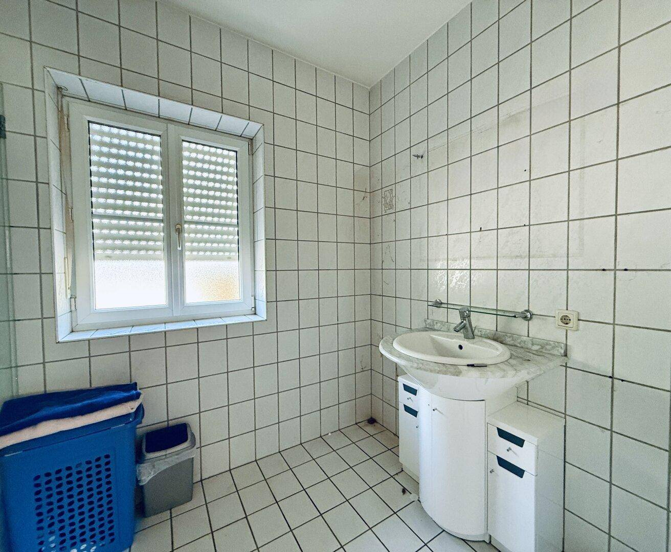 Badezimmer mit weißen Fliesen, Einzelwaschbecken und einem Fenster für Tageslicht.
